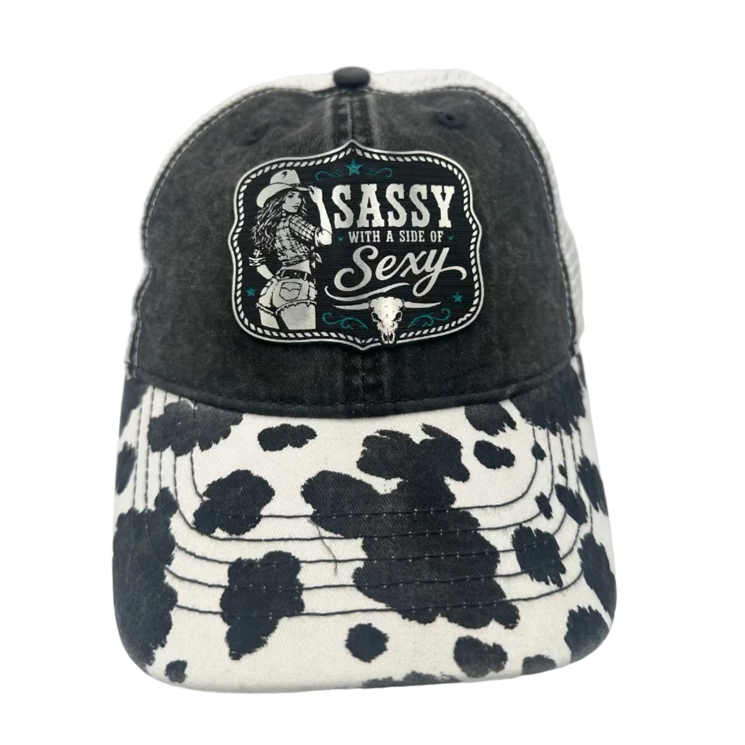 A distressed black trucker-style cap with a black-and-white cow-print brim and a front patch reading 'Sassy with a side of Sexy' with a cowboy illustration.